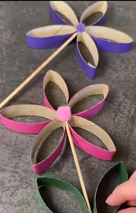 Bunte Papierblumen in Blau Rosa Gruen mit Stielen auf grauer Flaeche