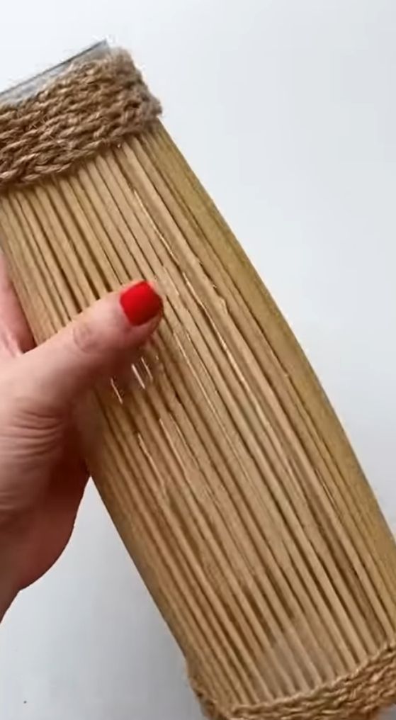 Hand mit rotem Nagellack hält beige Stäbe mit Juteband gebunden