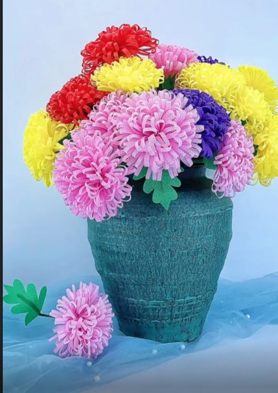 Bunter Pompon Blumenstrauss in blaugruner Vase auf blauem Tull