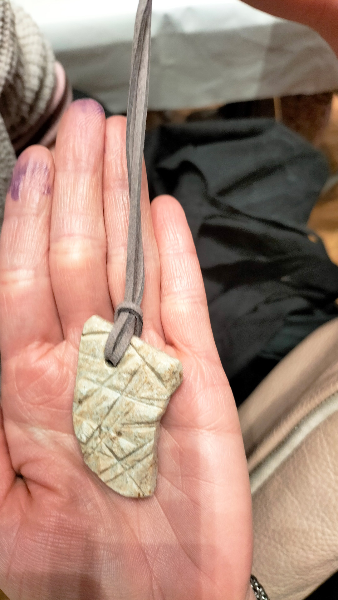 Hand haelt grauen Schnuranhanger mit hellgruenem Stein und Kerben