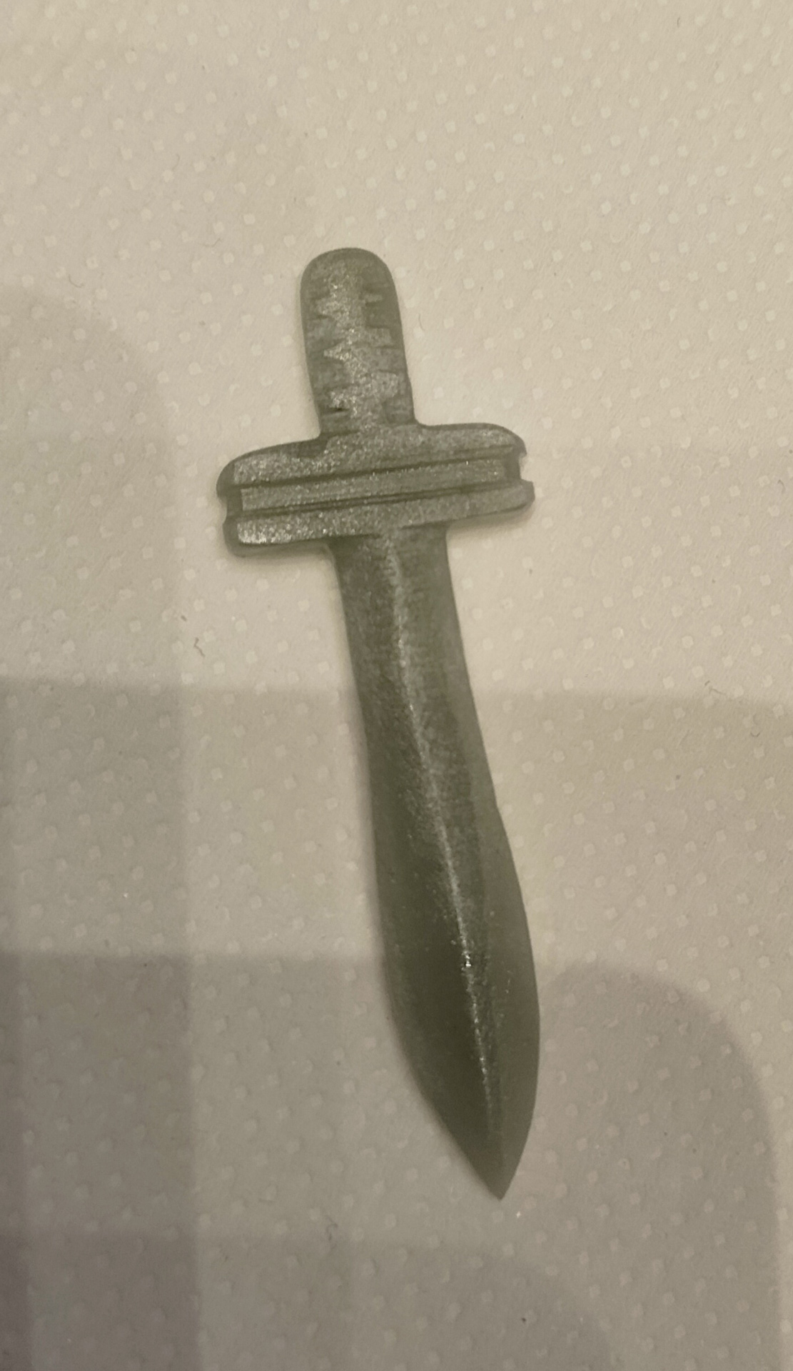 Grauer kleiner Spielzeugdolch aus Metall mit schlichtem Griff auf Stoff
