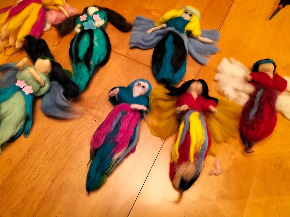 Sechs farbenfrohe Filzpuppen mit vielfältigen Frisuren und bunten Kleidern auf Holz