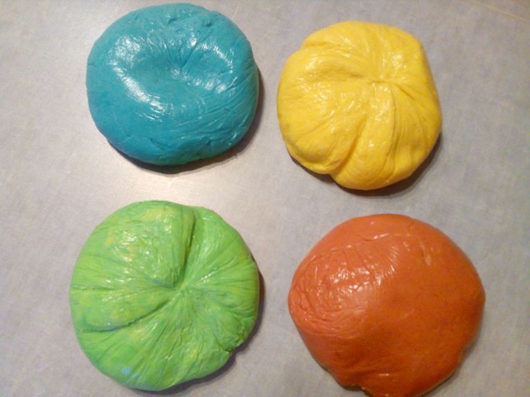 Vier bunte Teigstücke in Blau, Gelb, Grün und Orange liegen nebeneinander