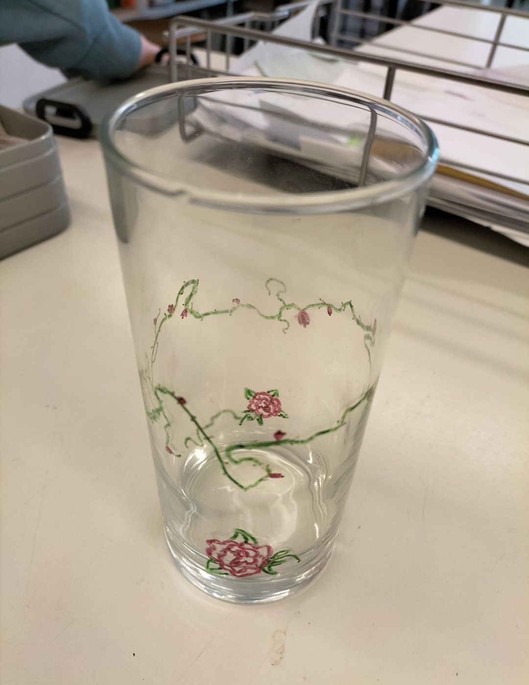 Transparentes Glas mit rosa Blumenmuster steht ruhig auf hellem Tisch