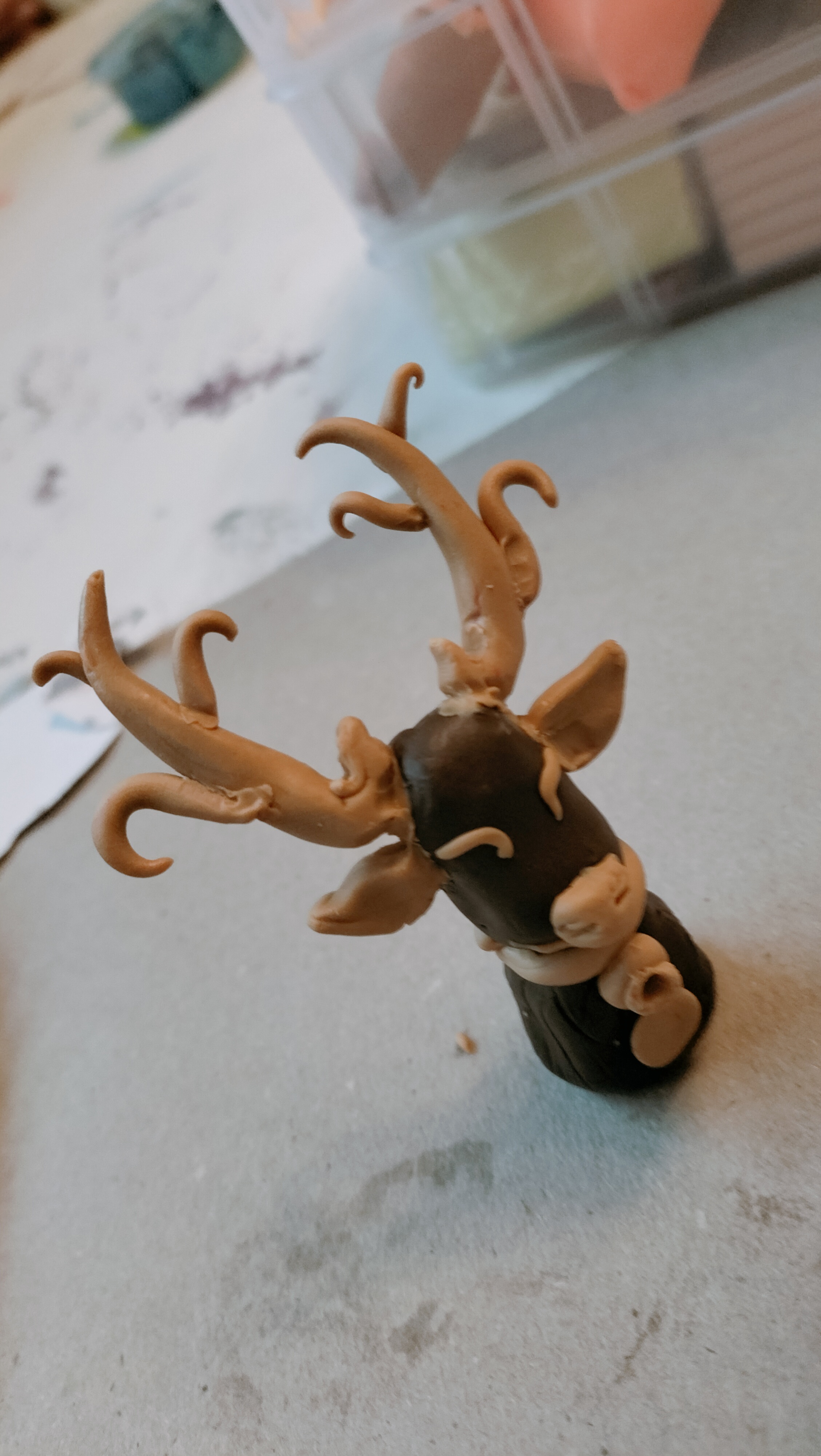 Braune Tonfigur eines Hirschkopfs mit schwarzen Details und geschwungenem Geweih wirkt verspielt auf blauem Tisch