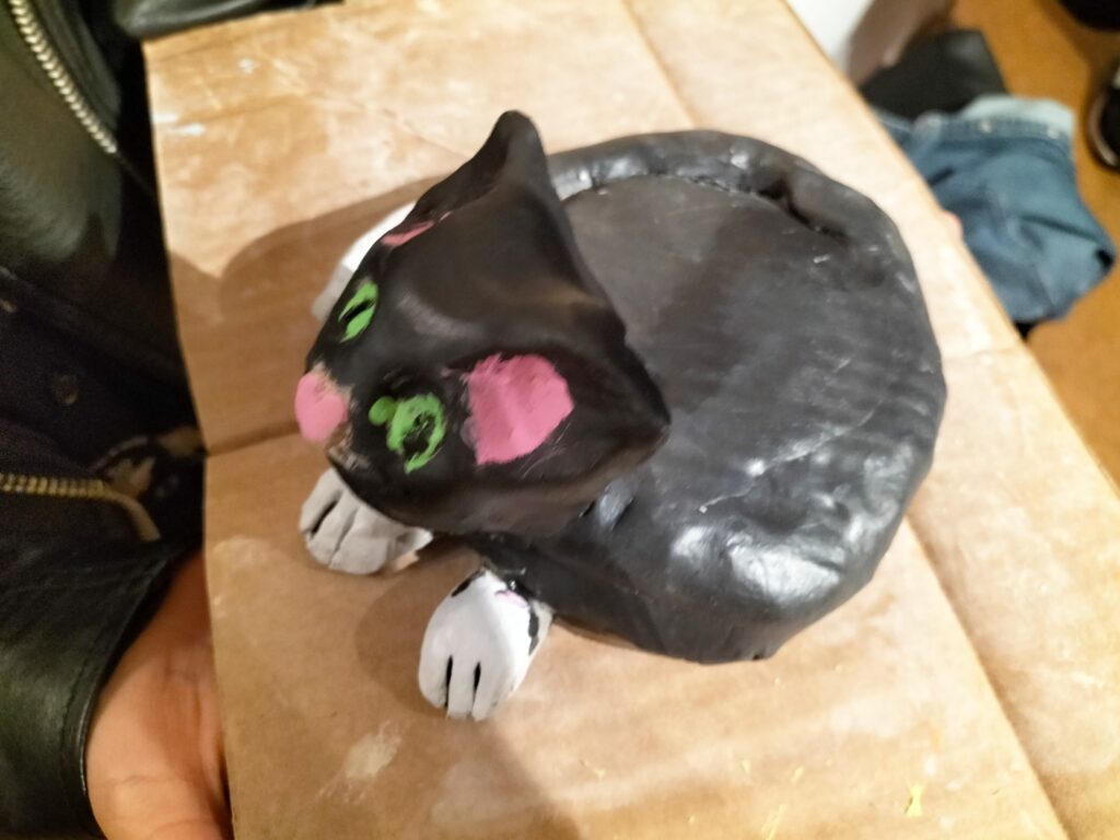 Schwarze Katzenfigur mit neugierigem Blick gruenen Augen und rosa Wangen